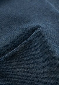 Mörkblått stickat tyg med en slät textur och subtilt, fint mönster. Har en liten ficka med något upphöjda kanter.