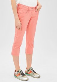 Pantalons capri roses en coton extensible, présentant des poches avant et une taille ajustée. Associés à des baskets colorées avec des accents métalliques.