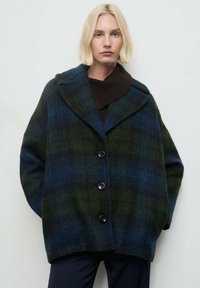 Cappotto a scacchi in blu scuro e verde, realizzato in un tessuto testurizzato. Presenta una silhouette oversize, rever ampi e quattro bottoni frontali.