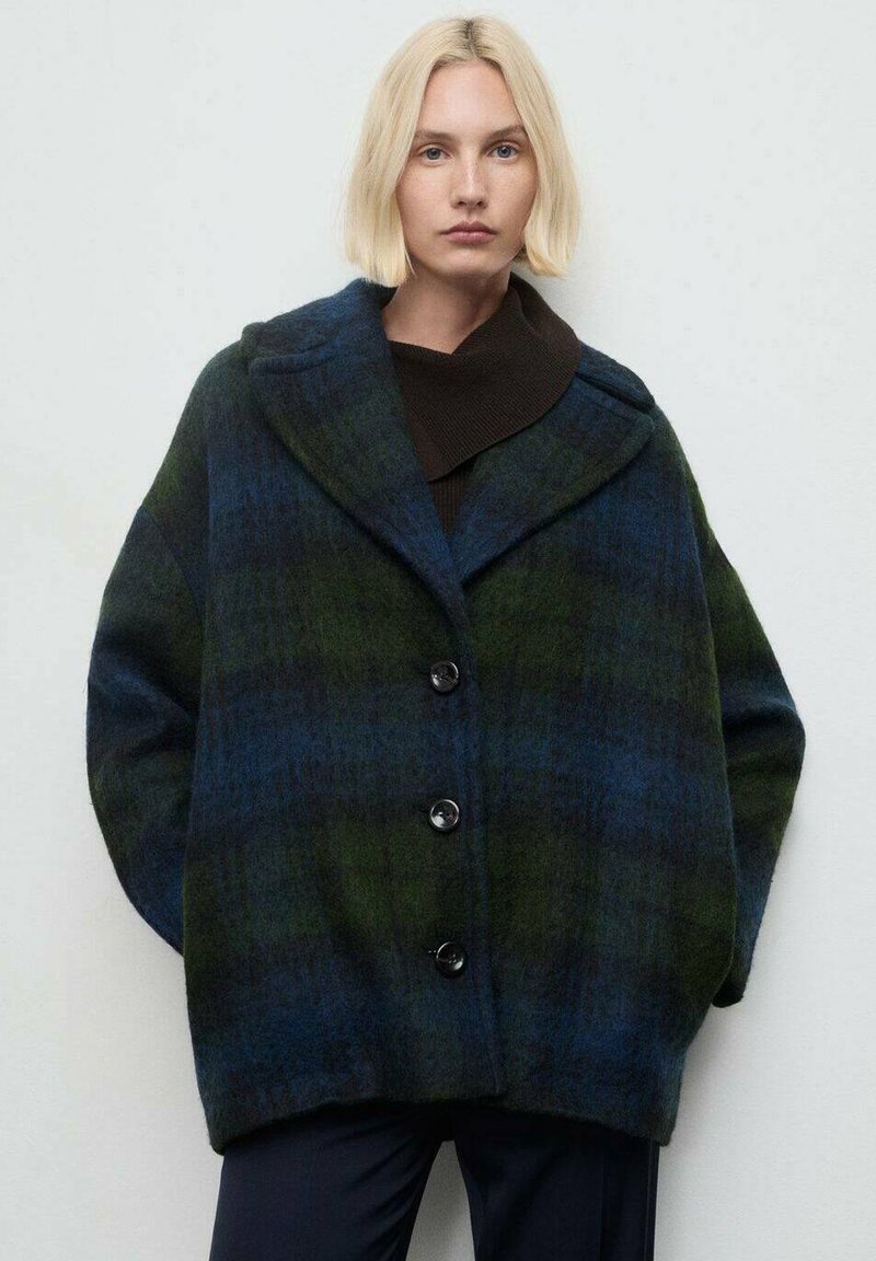 Cappotto a scacchi in blu scuro e verde, realizzato in un tessuto testurizzato. Presenta una silhouette oversize, rever ampi e quattro bottoni frontali.