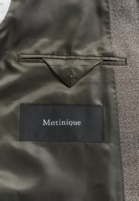 Tissu satin vert foncé avec une petite poche intérieure au-dessus d'une étiquette noire cousue avec le mot "Matinique" en texte blanc.