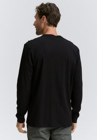 Zwarte longsleeve shirt van zacht katoen met een ronde hals, aangesloten mouwen en een rechte zoom; minimalistisch ontwerp zonder zichtbare patronen.