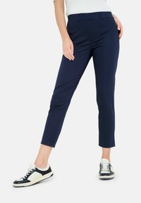 Navyblaue, eng geschnittene Hosen mit glatter Textur und verkürzter Länge, kombiniert mit schwarz-weißen Sneakers mit Schnürdesign.