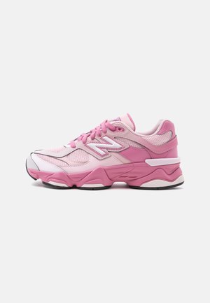 Baskets de sport roses et blanches avec des panneaux en mesh et cuir, des lacets, une semelle épaisse et rembourrée, et un logo latéral sur un fond uni.