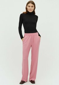 Must pikkade varrukatega kaelusega topp, mida on ühendatud heleroosade, lahtiste ja elastse vöökohaga pükstega. Märkimisväärsed detailid hõlmavad küljetaskuid ja sujuvat tekstuuri.