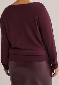Pull en tricot bordeaux avec un large décolleté et des manches longues, doté d'un ourlet ajusté. Associé à une jupe en cuir bordeaux assortie.