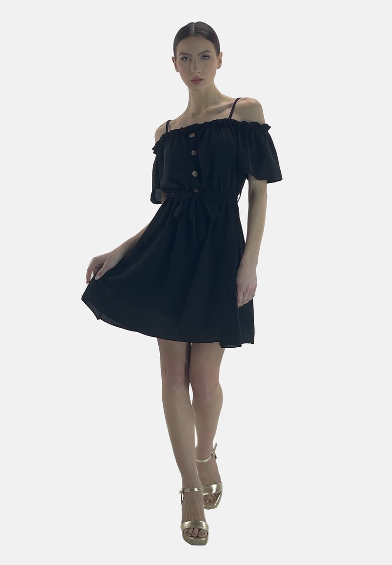 Vestido negro de hombros descubiertos con mangas acampanadas, detalles de botones y un lazo en la cintura. La textura parece suave; la longitud es por encima de la rodilla. Tacones dorados.