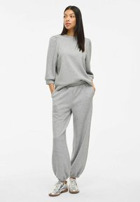Grau geschnittener Trainingsanzug mit einem lässig geschnittenen Pullover mit Puffärmeln und passenden elastischen Hosen. Die Schuhe sind metallisch mit einem gemusterten Design.