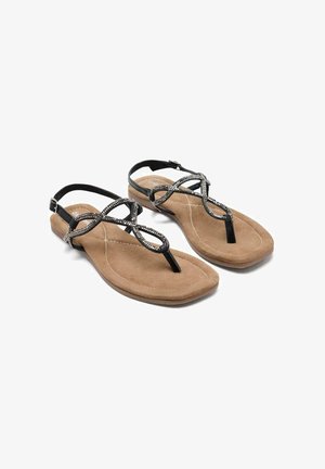 Sandalias negras de tiras con un acento metálico decorativo, que cuentan con una plantilla suave de color tan y una suela plana, diseñadas para la comodidad y el uso casual.