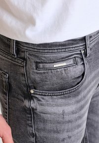 Grå denimjeans med en blekt effekt, som har framfickor, en liten ficka och metallspikar på sidsömmarna.