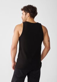 Top a canotta nero a coste con ampie aperture per le braccia, design semplice e texture morbida. Vista della schiena del modello che mette in mostra la muscolatura e i tatuaggi.