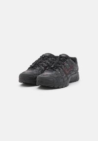 Sapatilhas Nike negras com material em malha texturizada e uma sola sobressaíngue. Apresentam atacadores elásticos e um logo Swoosh numa tonalidade vinho.