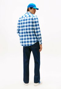Blauw-wit geruite overhemden met knopen, spijkerbroek en een blauwe pet. Het shirt heeft lange mouwen en een gebogen onderrand. Witte sneakers.