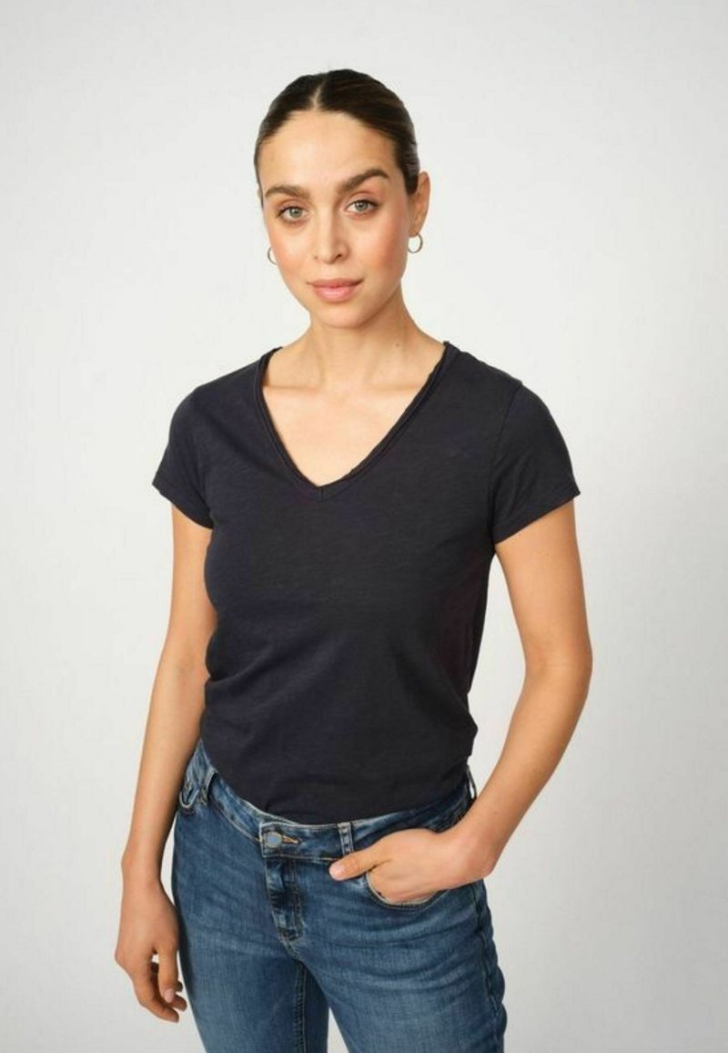 Temno modra v-neck majica s kratkimi rokavi, narejena iz mehke tkanine, kombinirana z modrimi kavbojkami. Majica ima sproščen kroj in preprost dizajn.