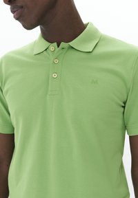 Grön polo shirt med en klassisk design, krage, tre knappar och ett subtilt strukturmaterial. Litet logotyp på vänster bröst.