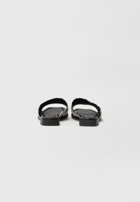 Schwarze flache Sandalen mit einer strukturierten Oberseite, schmalen Riemen und einem quadratischen Zehendesign. Die Sohle ist flach mit einem leicht erhöhten Absatz.