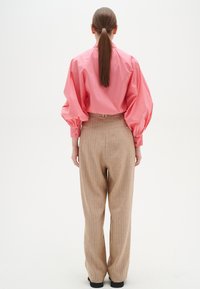 Blusa rosa a maniche lunghe con maniche a sbuffo; pantaloni beige a righe verticali; modello di spalle; tessuto liscio, vestibilità sartoriale.