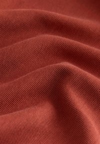 Tkanina tekstylna w głębokim rdzawej barwie, charakteryzująca się miękką, gładką fakturą z drobnym wzorem dzianiny i delikatnym uk�ładem.