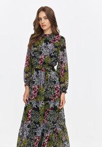 Long dress featuring black fabric with floral patterns in green, pink, and white. Puff sleeves, waist tie, and tiered skirt design.