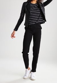 Giacca da motociclista in pelle nera, maglietta a righe bianche e nere, pantaloni slim-fit neri e sneakers bianche. Texture liscia, design casual.