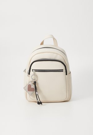 Lille cremefarvet rygsæk med lynlåslomme foran og en nøglering med et syet rødt hjerte samt sorte snore med sølvperler.