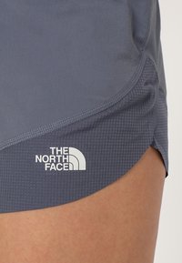 Harmaat urheilusortsit, joissa on tekstuuri ja sivurako, sekä valkoinen "The North Face" -logo helman kohdalla.