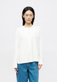 Bílá, volná blůza s dlouhými rukávy, kulatým výst�řihem a jemným rozparkem vpředu. Kombinována se světle modrými, vysokými džíny.