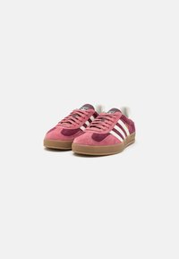 Zapatillas de ante en rosa y burdeos oscuro con rayas blancas. Cuentan con una puntera redonda, diseño de cordones y suela de goma beige.