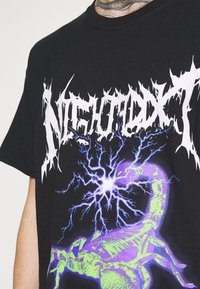 Camiseta negra con el texto desgastado en blanco "NIGHTXX" y una imagen luminosa de un escorpión púrpura con acentos azul eléctrico.