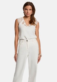 Blouse blanche avec des accents en dentelle et un col en V, associée à un pantalon large taille haute de couleur claire. Tissu lisse, design minimaliste.