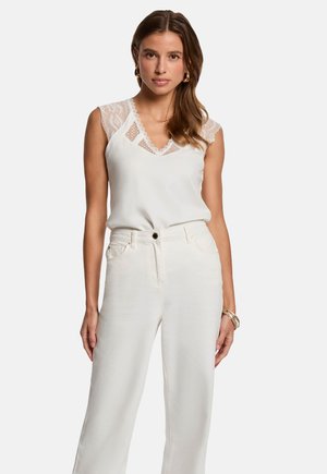 White blouse with lace accents and a V-neckline, paired with high-waisted light-colored wide-leg trousers. Smooth fabric, minimalist design.
