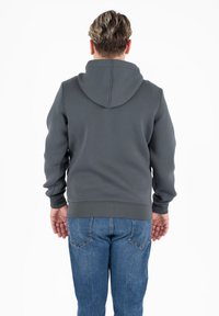 Grijze hoodie van zacht materiaal, voorzien van een kangoeroe-pocket, geribde manchetten en onderrand, gedragen bovenop blauwe jeans.