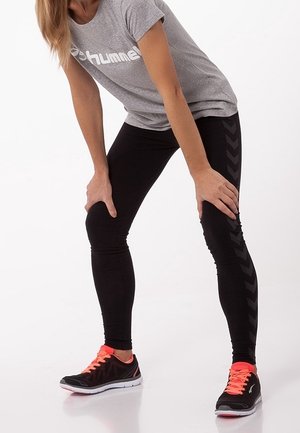 Šedé tričko s logem, černé legíny s chevronovým vzorem a černé tenisky se zářivě růžovými tkaničkami. Hladká tkanina a úzký střih.