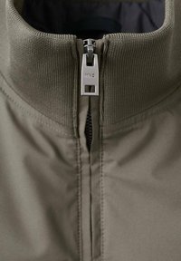 Chaqueta verde oliva con un alto cuello, que cuenta con un zipper completo y un tirador metálico. Tela texturizada con acentos acanalados.