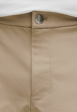 Béžové kalhoty z látky s rovnou přední částí, zapínáním na knoflíky a švy po stranách. Hladká textura s minimálním zdobením.