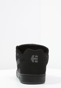 Schwarze Skate-Schuhe mit einer glatten Wildlederoberfläche, gepolstertem Kragen und einer strukturierten Gummisohle. Mit grauem Logo und seitlichen Streifen.