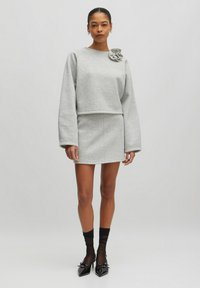 Grijze sweatshirts met een ronde hals en bloemenaccent, gecombineerd met een bijpassende grijze minirok; het model draagt zwarte hoge hakken en legging.