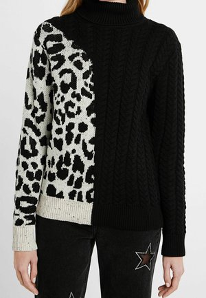 Pull à col roulé avec une moitié en tricot torsadé noir et une moitié imprimé léopard noir et blanc, porté avec un jean noir orné d'étoiles en strass.