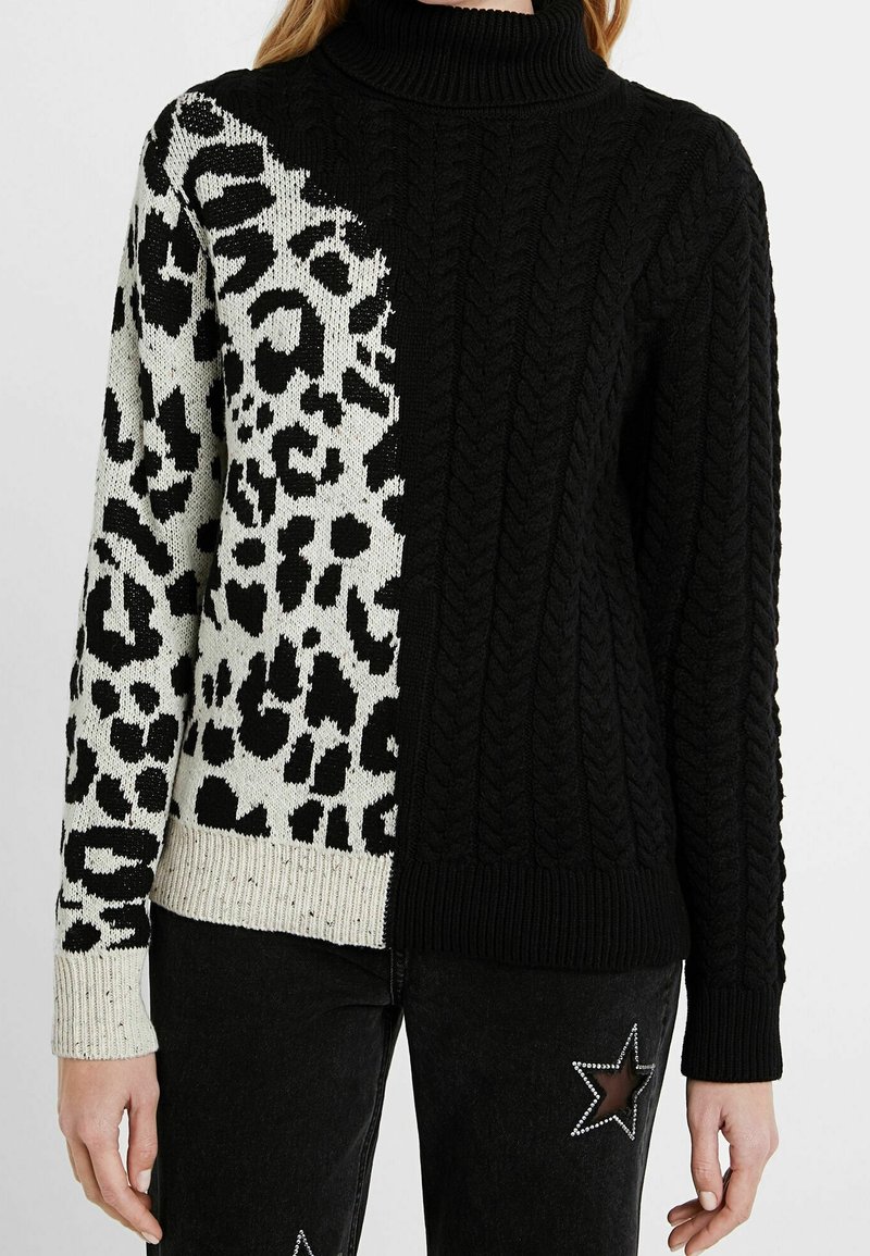 Pull à col roulé avec une moitié en tricot torsadé noir et une moitié imprimé léopard noir et blanc, porté avec un jean noir orné d'étoiles en strass.