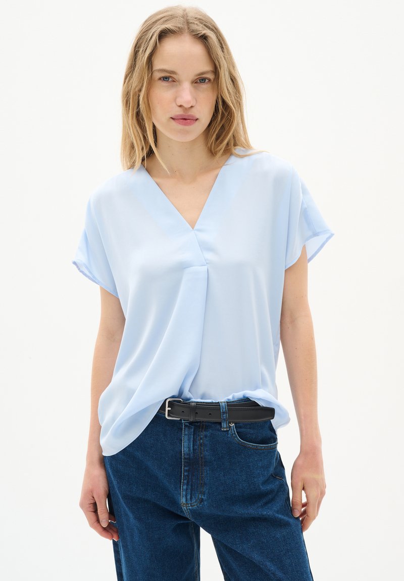 Blusa azzurro chiaro, a maniche corte con scollatura a V e leggera drappeggiatura. Abbinata a pantaloni in denim scuri, dal fit rilassato e una cintura nera.