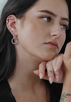 Silberne Creolen mit einem verdrehten Design, die zusammen mit kleinen Steckerohrringen in einem Nahaufnahme-Porträt einer Person gezeigt werden.