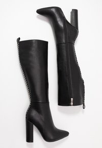 Para czarnych kozaków do kolan na obcasie z zakończeniem w szpic, z bocznym zamkiem błyskawicznym i białymi detalami ściegów wzdłuż tylnego szwu.