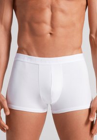 Hvide boksertrusser lavet af glat stof, med en tætsiddende pasform, en elastisk taljeelastik med diskret branding og en frontåbning.