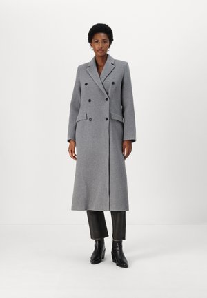 Manteau gris croisé avec revers à cran, poches latérales et silhouette droite, associé à un pantalon noir ajusté et des bottes à talons.