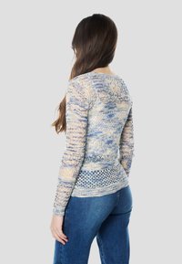 Könnyű, áttetsző pulóver világoskék és bézs színben, bonyolult mintákkal. Hosszú ujjú, kerek nyakkivágású, texturált kötött részletekkel.