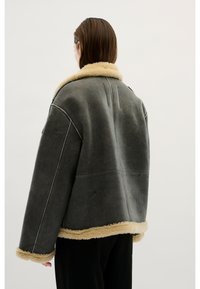 Chaqueta de piel vuelta gris con un suave cuello de piel marrón claro, que presenta mangas extragrandes y costuras visibles. El material tiene un acabado mate.