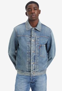 Jachetă din denim albastru deschis, cu închidere butonată, guler ascuțit, buzunar pe piept și buzunare laterale. Finisaj uzat cu detalii de cusătură vizibile.