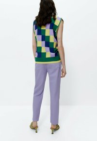 Chaleco de punto en un patrón de cuadros en verde, azul, amarillo y púrpura; combinado con pantalones lavanda y zapatos de tacón verdes. Mangas cortas, ajuste casual.