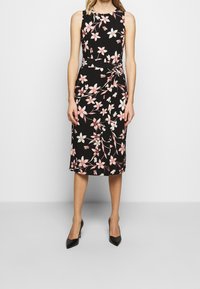 Svart ärmlös klänning med blommönster i rosa och vitt, med en knutdetalj i midjan och en knälång fåll.