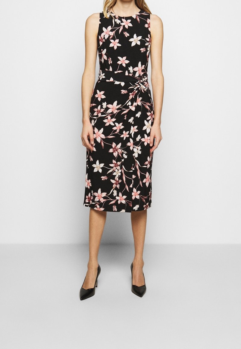 Svart ärmlös klänning med blommönster i rosa och vitt, med en knutdetalj i midjan och en knälång fåll.